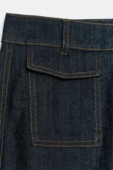 Pantalon tipo culotte de tiro alto confeccionado en denim azul oscuro. Presenta pernera ancha y corta, bolsillos delanteros de plastrón con solapa, falsos bolsillos traseros de vivo y costuras en contraste. Cierre frontal con cremallera y botón.
