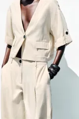 Chaqueta corta de escote en pico con cierre frontal de un botón. Presenta mangas cortas con detalle de vuelta, trabilla y botón, además de falsos bolsillos delanteros con solapa.