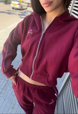 Campera tipo hoodie con cierre frontal, de corte cropped y color bordó. Presenta detalles de líneas blancas en las mangas y un bordado pequeño en el pecho.