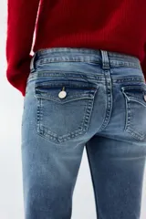 Jean de denim elástico color celeste claro, de tiro bajo y corte acampanado desde la rodilla. Cuenta con bolsillos abiertos delanteros, bolsillos traseros con solapa y botón, y cierre frontal con cremallera y botón metálico.