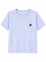 Remera blanca con estampado frontal de la leyenda "OUT OF OFFICE", un sol amarillo y ondas rosadas, acompañada por el texto "slow living by the sea".