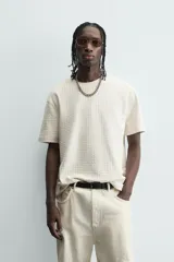 Camiseta de manga corta color crema, con cuello redondo y tejido texturizado con estructura.