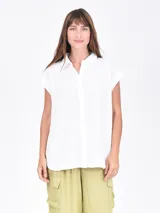 Camisa blanca de manga corta, con cuello camisero y botones frontales. Presenta un corte recto y holgado.