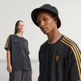 Camiseta de fútbol Adidas del Manchester United, modelo Terrace Icons. Diseño negro con sutiles rayas verticales moradas, franjas amarillas en los hombros y detalles bordados en dorado, incluyendo el trébol de Adidas y el escudo clásico del club.