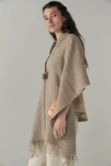 Chal de lana fina sin teñir con diseño de cuadros sutiles, cierre frontal con alamar y bolsillos de cuero metalizado. Presenta terminaciones con flecos en el ruedo y un calce estructurado en los hombros.