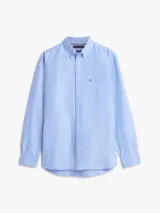 Camisa Tommy Hilfiger de corte regular en puro algodón Oxford, color celeste con sutiles rayas diplomáticas. Presenta cuello con botones, bolsillo de parche en el pecho con el logo bordado y mangas largas con puños redondeados.