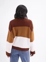 Buzo de tejido de punto con diseño de bloques horizontales en tres colores: marrón oscuro, marrón claro y blanco. Presenta cuello redondo y mangas largas con calce relajado.