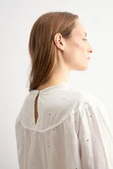 Blusa blanca de algodón con diseño de encaje bordado tipo broderie en el cuello, mangas y ruedo. Presenta mangas tres cuartos acampanadas y un corte holgado.
