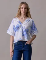 Blusa blanca estampada con flores azules, escote en V y mangas cortas amplias. Detalles de puntilla en escote y mangas.