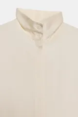 Camisa fluida de tejido satinado con cuello alto y manga larga terminada en puño ancho. Presenta cierre frontal con botones ocultos y bajo recto.