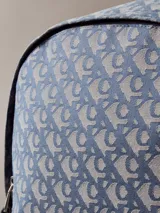 Mochila de poliéster reciclado con estampado de logo jacquard en tonos azul y gris. Presenta asa de mano superior, correas acolchadas ajustables, cierre de cremallera y bolsillo frontal con cremallera.