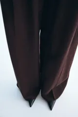 Pantalón sastrero de tiro alto color marrón, de corte recto y amplio, confeccionado en mezcla de lino y viscosa. Cuenta con trabillas para cinturón, cierre frontal oculto con botón y bolsillos laterales.