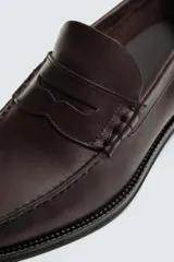 Mocasín de vestir fabricado en piel color marrón oscuro, con detalle de antifaz en el empeine, plantilla de piel y suela a contraste con ligero tacón.