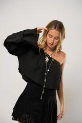 Blusa negra con un hombro descubierto y manga larga con volados.