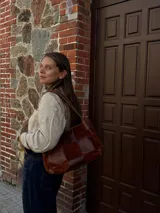 Cartera de hombro confeccionada en cuero y gamuza con diseño de damero, combinando paneles de texturas lisas y aterciopeladas. Presenta una manija trenzada y detalles de costuras artesanales en los laterales.