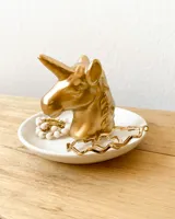 Despojador con forma de cabeza de unicornio dorado sobre una base blanca.