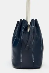 Bolso de hombro tipo saco confeccionado en piel azul marino, con detalle de pespuntes blancos verticales, asas finas de hombro en color blanco y cierre fruncido.