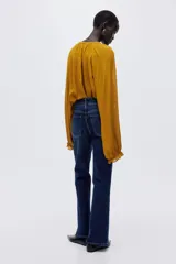 Jean de tiro alto con corte acampanado desde la rodilla. Presenta cierre frontal con doble botón, bolsillos frontales decorativos con solapa y botón, y bolsillos traseros tipo parche.