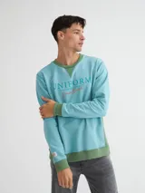 Buzo celeste con cuello redondo y puños en verde, con estampa frontal con la palabra "Uniform" en celeste y "Denim Brand" en naranja.