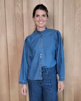 Camisa de denim con cuello alto tipo mao con volados, cierre frontal con botones y mangas largas con puños elásticos con volados.