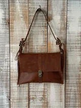 Cartera de cuero color marrón con diseño rectangular, solapa frontal con cierre metálico a presión y correa ajustable con detalles de nudos decorativos en los extremos.