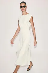 Vestido midi de crepe color blanco marfil, sin mangas, con cuello redondo y corte en la cintura. Falda con vuelo evasé y cierre lateral con cremallera oculta.