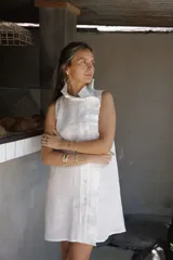 Vestido corto de lino sin mangas, con cuello alto adornado con un volado. Presenta un acceso frontal cruzado con botones forrados en la misma tela y un largo por encima de la rodilla.