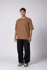 Remera oversize de algodón color beige, de manga corta y cuello redondo, con pequeño estampado frontal de la marca en tono bordó.