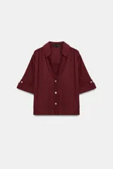 Camisa bordó con textura, cuello solapa, escote en V y manga corta con vuelta y trabilla. Cierre frontal con botones nacarados.