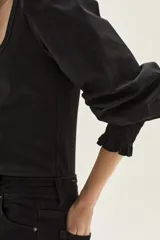 Top de calce ajustado color marrón, con escote cuadrado y mangas largas abullonadas de tela lisa. Los puños de las mangas son elastizados.