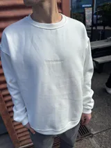 Buzo de corte oversize en color blanco, confeccionado en algodón, con cuello redondo y detalle de logo bordado en el centro del pecho.