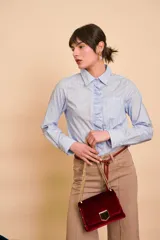 Camisa celeste con rayas blancas verticales, de manga larga, cuello camisero y detalles de volados frontales.