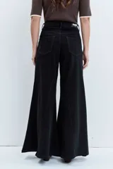 Jeans de tiro alto en color negro, con diseño de corte acampanado y paneles godet que aportan amplitud en el bajo. Presenta costuras visibles y cierre frontal con botón y cremallera.