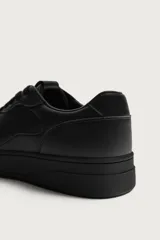 Zapatillas deportivas de estilo retro, color negro, con diseño superior de paneles combinados, cordones al tono y suela gruesa con volumen.
