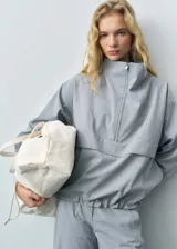Anorak de diseño oversize en color gris, con cuello chimenea y cierre frontal de cremallera. Presenta mangas largas y ruedo elástico, confeccionado en tejido con acabado estructurado.