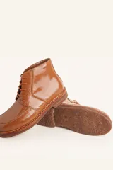 Bota acordonada de cuero vacuno con acabado charol color suela, con suela de goma tipo crepe y costuras reforzadas.
