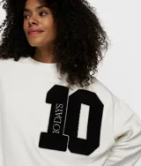 Suéter de felpa de algodón color blanco roto, de corte oversize y cuello redondo. Presenta un gran parche aplicado en el pecho con el número '10' en negro, con la palabra '10DAYS' verticalmente en el lado izquierdo del número.