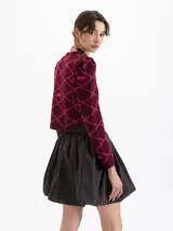 Saco tipo cardigan corto tejido en jacquard con diseño gráfico de labios y cadenas. Presenta cuello redondo, mangas largas con hombros ligeramente abullonados y cierre frontal con botones.