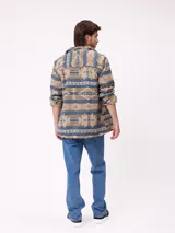 Camisa de manga larga con diseño de estampado étnico en tonos azules y beige. Presenta cuello clásico, cierre frontal con botones y bolsillos en el pecho.