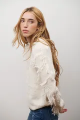 Buzo de punto color beige con cuello redondo, mangas largas con flecos decorativos y diseño de trenzas en el frente.
