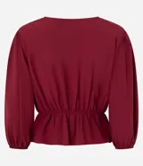 Blusa color vino tinto, con escote cruzado en V, mangas tres cuartos abullonadas con elástico en el puño y peplum ajustado en la cintura con lazo regulable.