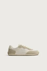 Zapatilla deportiva estilo barefoot, color marrón, con diseño de paneles en combinación de materiales y detalles en serraje. Cuenta con puntera redondeada y ancha, cordones en color crema y suela fina de goma flexible en contraste.