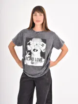 Remera de algodón con efecto acid wash en color gris oscuro, de corte holgado y manga corta. Presenta una estampa fotográfica en blanco y negro en el frente con la frase 'BLIND LOVE'.