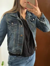 Campera de jean azul de corte clásico y largo a la cintura, con bolsillos frontales con solapa y botones metálicos.