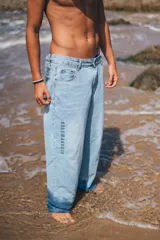Pantalón de jean corte loose fit color celeste claro, con diseño de cinco bolsillos y estampa vertical con la frase 'GLASSYWAVES' en la pierna derecha.