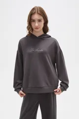 Canguro de corte holgado en color gris oscuro, con capucha y mangas largas. Presenta un detalle de letras bordadas con brillos en el centro del pecho.