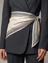 Pañuelo triangular de satén con estampado geométrico en tonos crema y negro. Presenta bordes definidos con patrones lineales y un acabado suave y brillante.