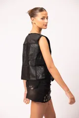 Pollera de jean negro con efecto de lavado localizado, terminación desflecada en el ruedo, tachas cuadradas en la cintura, apliques de alfileres de gancho en el bolsillo y ojalillos metálicos decorativos en la parte inferior.