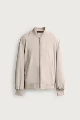 Cazadora tipo bomber ligera confeccionada en tejido técnico color beige, con cuello, puños y ruedo en rib elástico, cierre frontal con cremallera y bolsillos laterales de vivo.