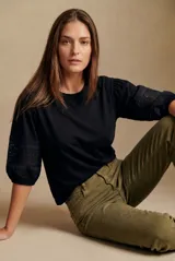 Remera negra de algodón con cuello redondo y mangas tres cuartos abullonadas, que presentan detalles de encaje y bordado inglés en la parte inferior.